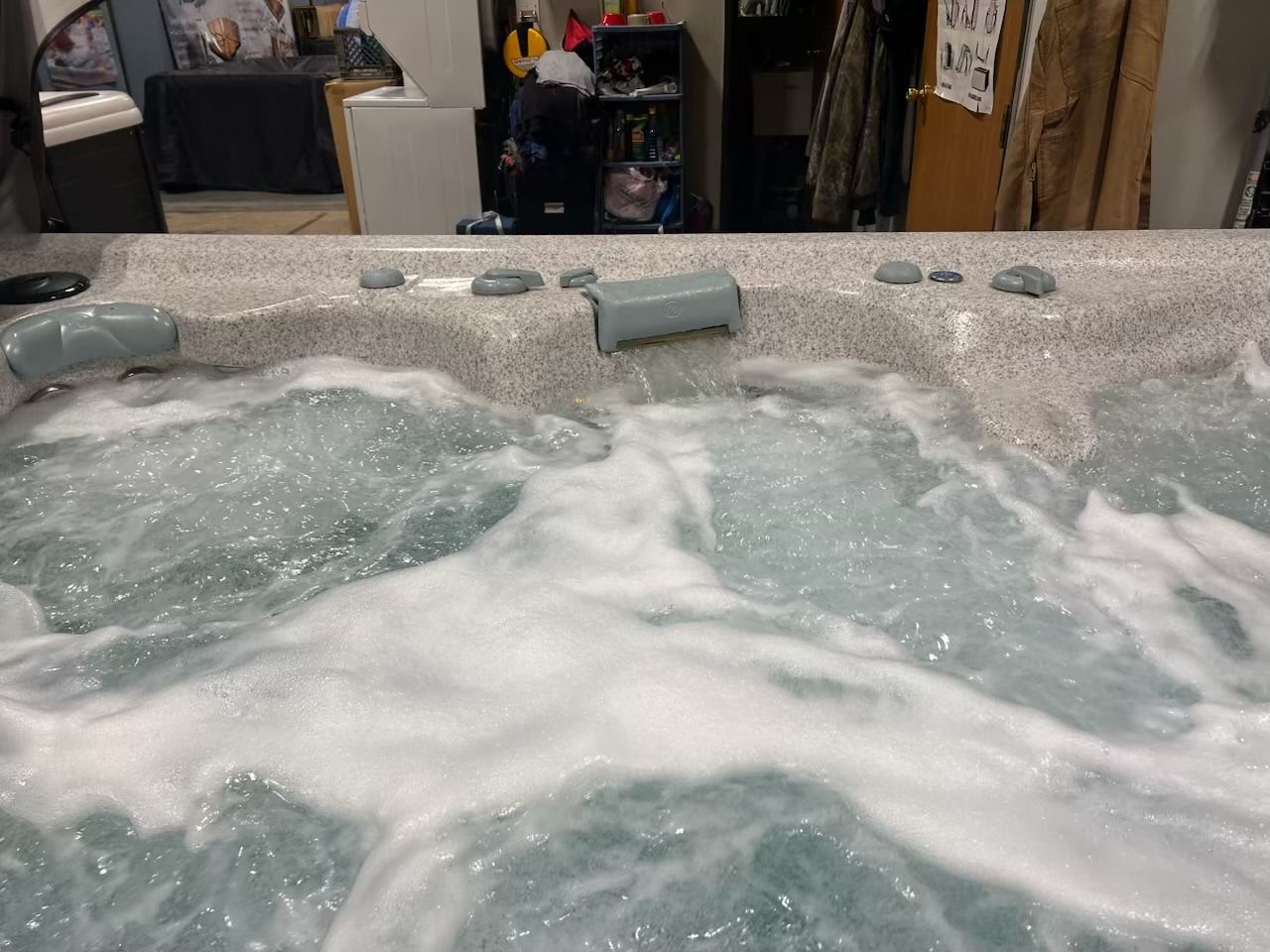 Bubbling hot tub with gray and speckled trim, indoors. Jets create foamy water.