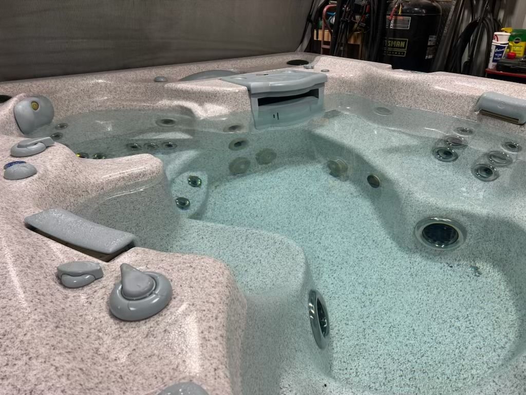 A hot tub with water and jets. Light-colored tub interior with gray controls and a partially open cover.