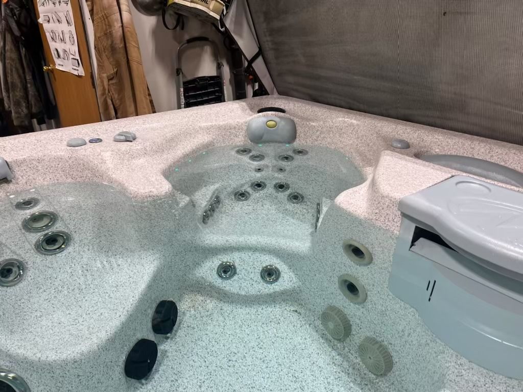Hot tub filled with water, multiple jets, light speckled interior, control panel on side.