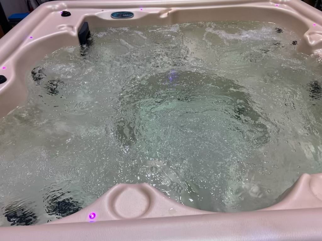 A hot tub filled with bubbling water, beige colored interior.