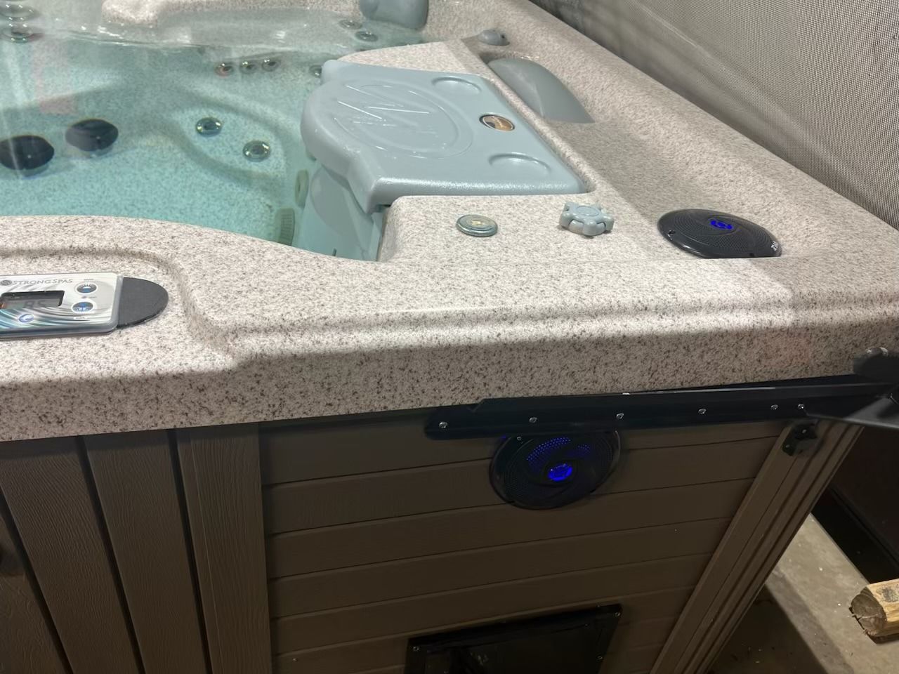 Hot tub with tan-colored surround, control panel, blue lights, and water.