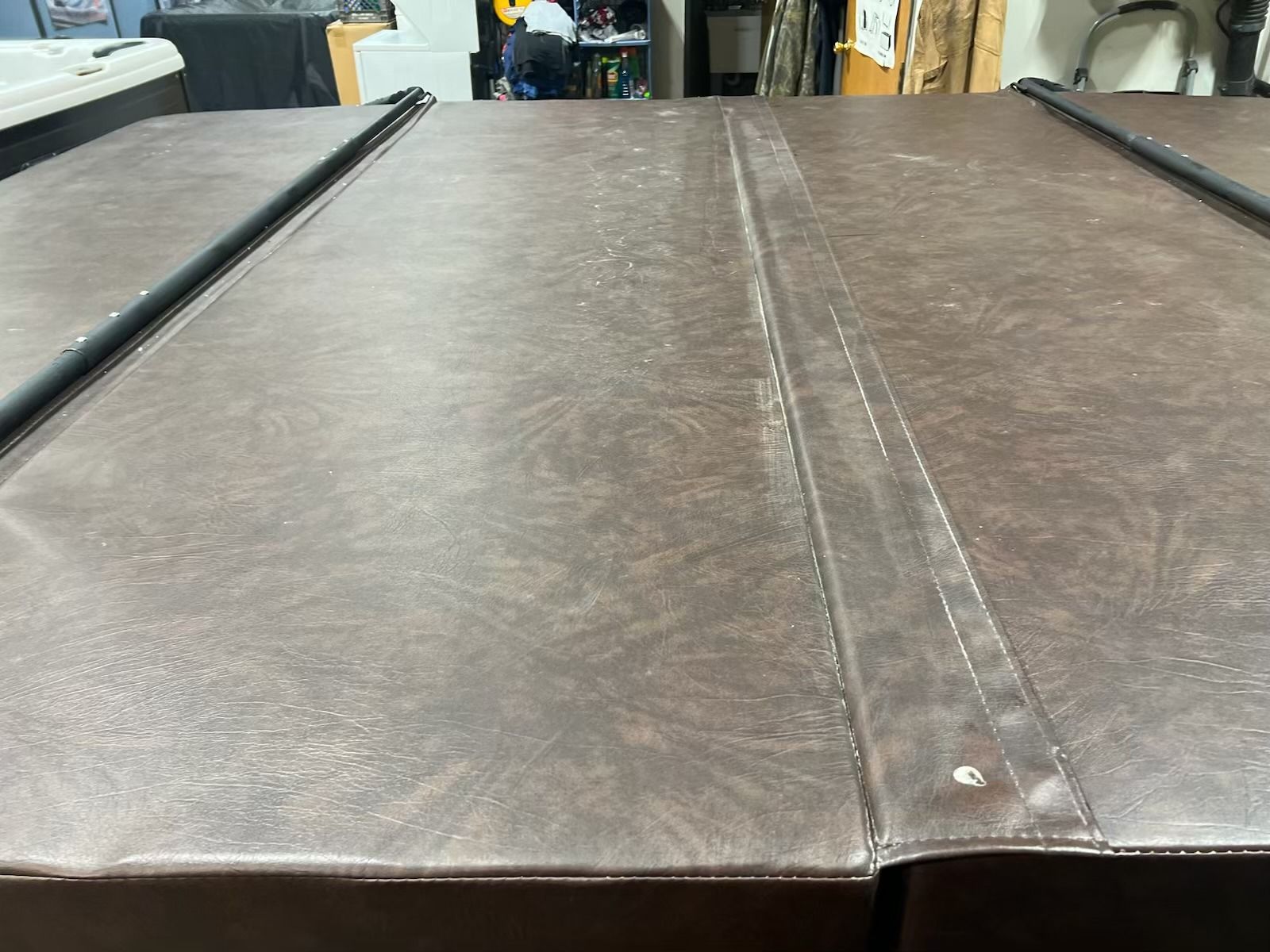 Brown spa cover, close-up, outdoors. Surface shows wear, seam down center, black supports.