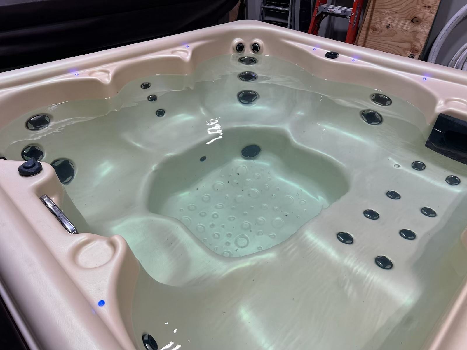 A beige hot tub filled with clear water, featuring several jets and a control panel.