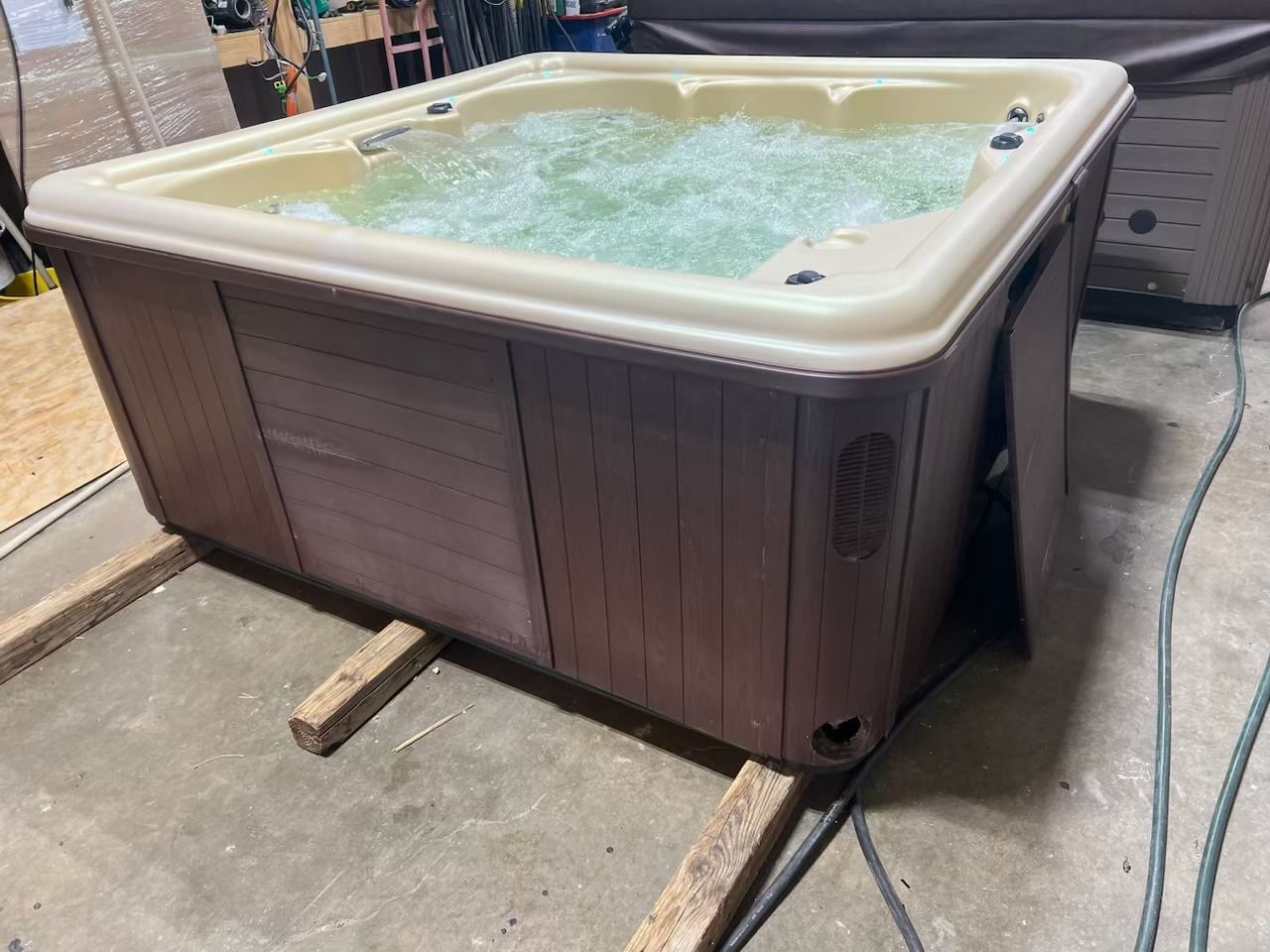 Hot tub with brown panels and beige top, filled with bubbly water, resting on wood supports.