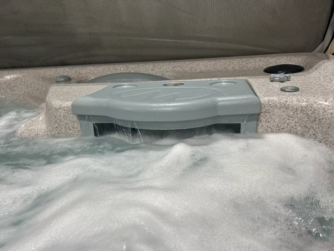 Hot tub with water cascading from a gray waterfall feature. Bubbles and jets are visible.
