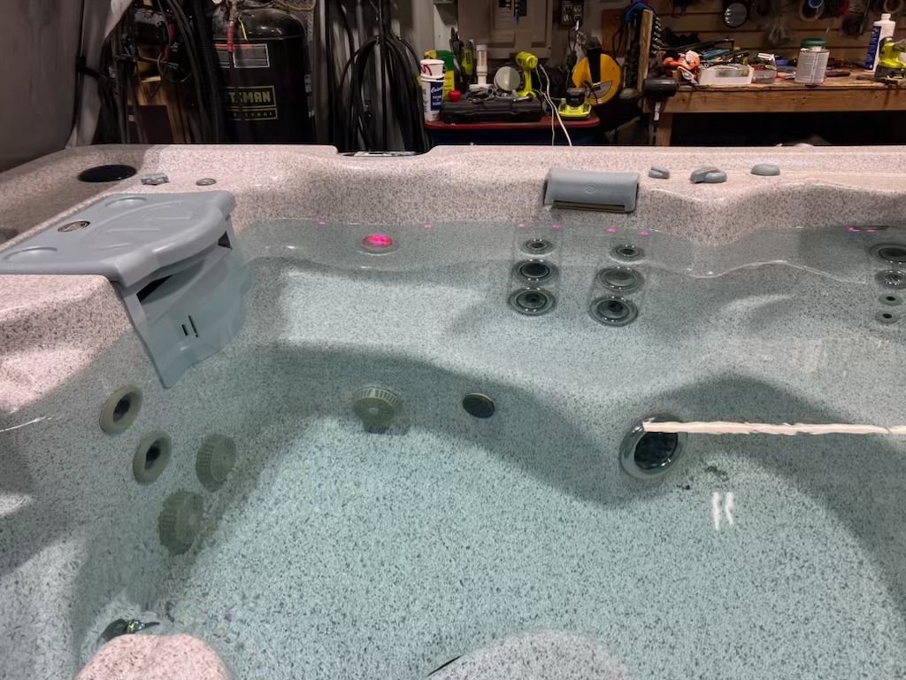 A hot tub filled with water, with jets and a cover, indoors near tools.