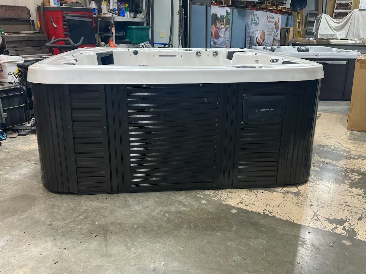 Black hot tub with white trim, indoors, on a concrete floor.