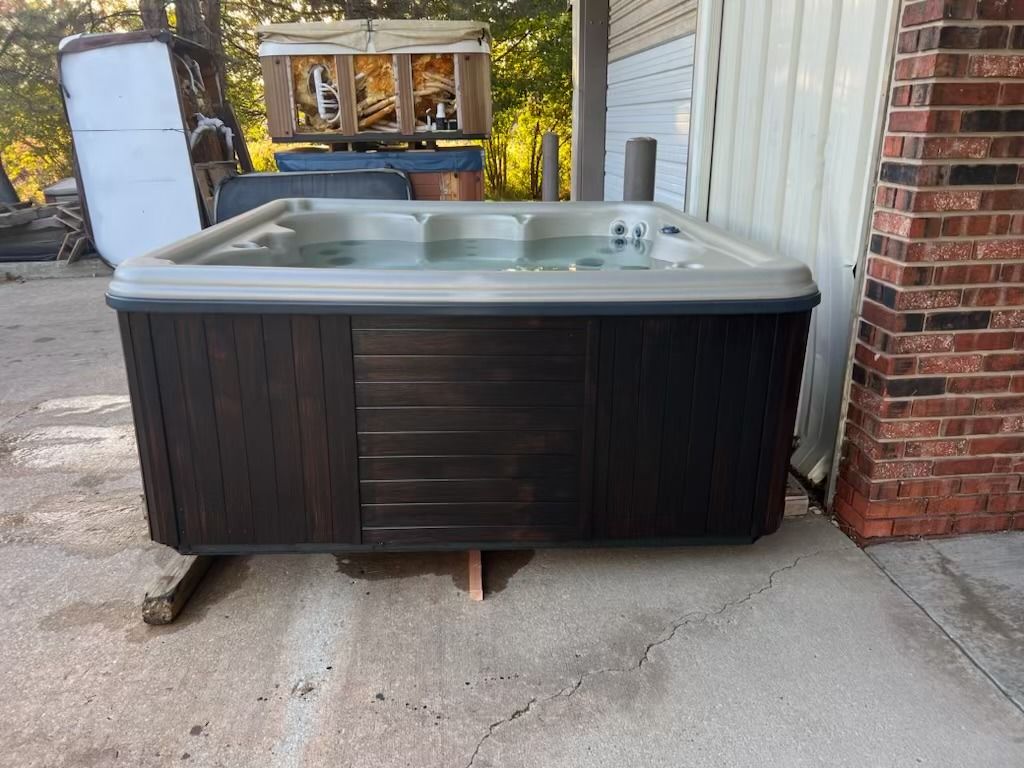 Hot tub with dark wood paneling, placed outside near a brick wall and other items.
