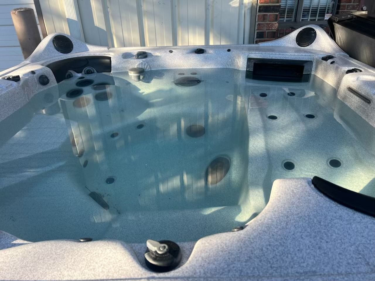 A filled hot tub with jets, gray shell, and clear water, outdoors in sunlight.