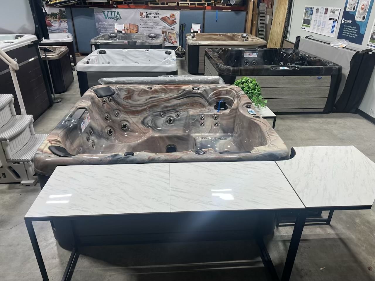 Hot tub showroom featuring a brown and cream spa with an attached white tabletop, surrounded by other hot tubs.