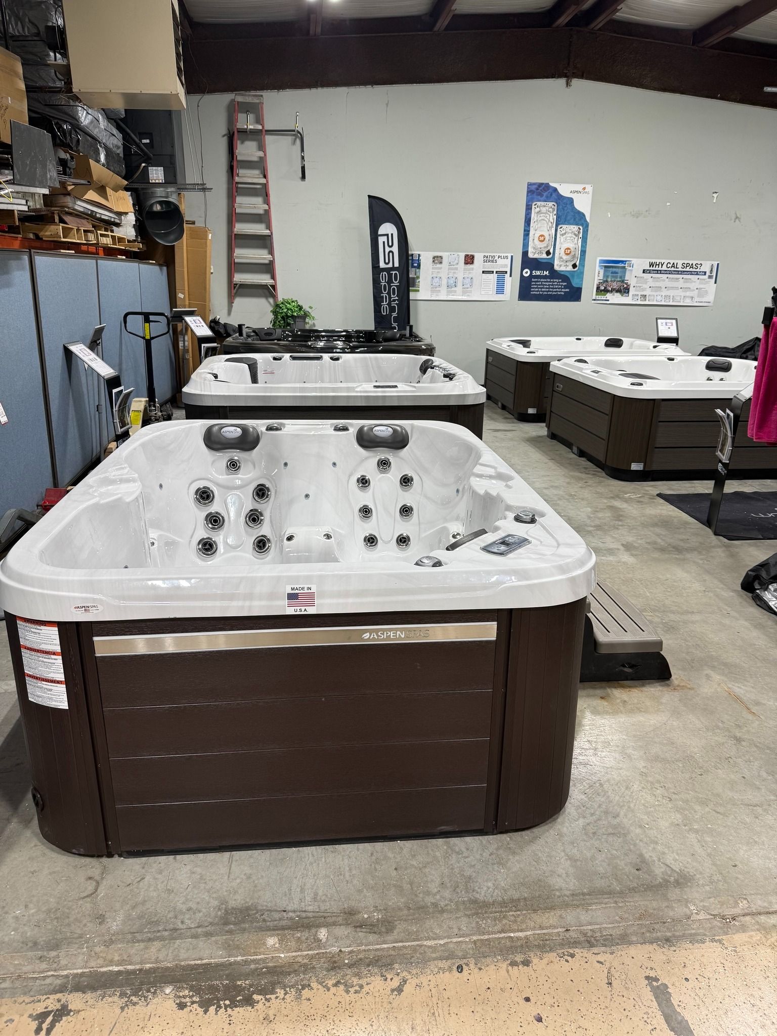 Hot tubs displayed in a warehouse setting, with various models and brown/white color schemes.