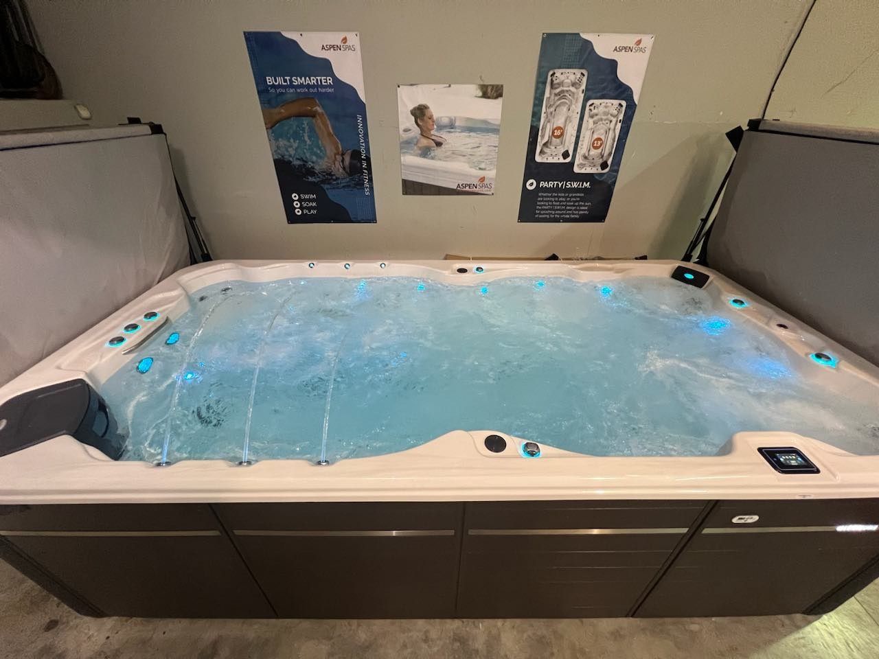 Hot tub with blue water and lights, brown cabinets, under posters on a wall.
