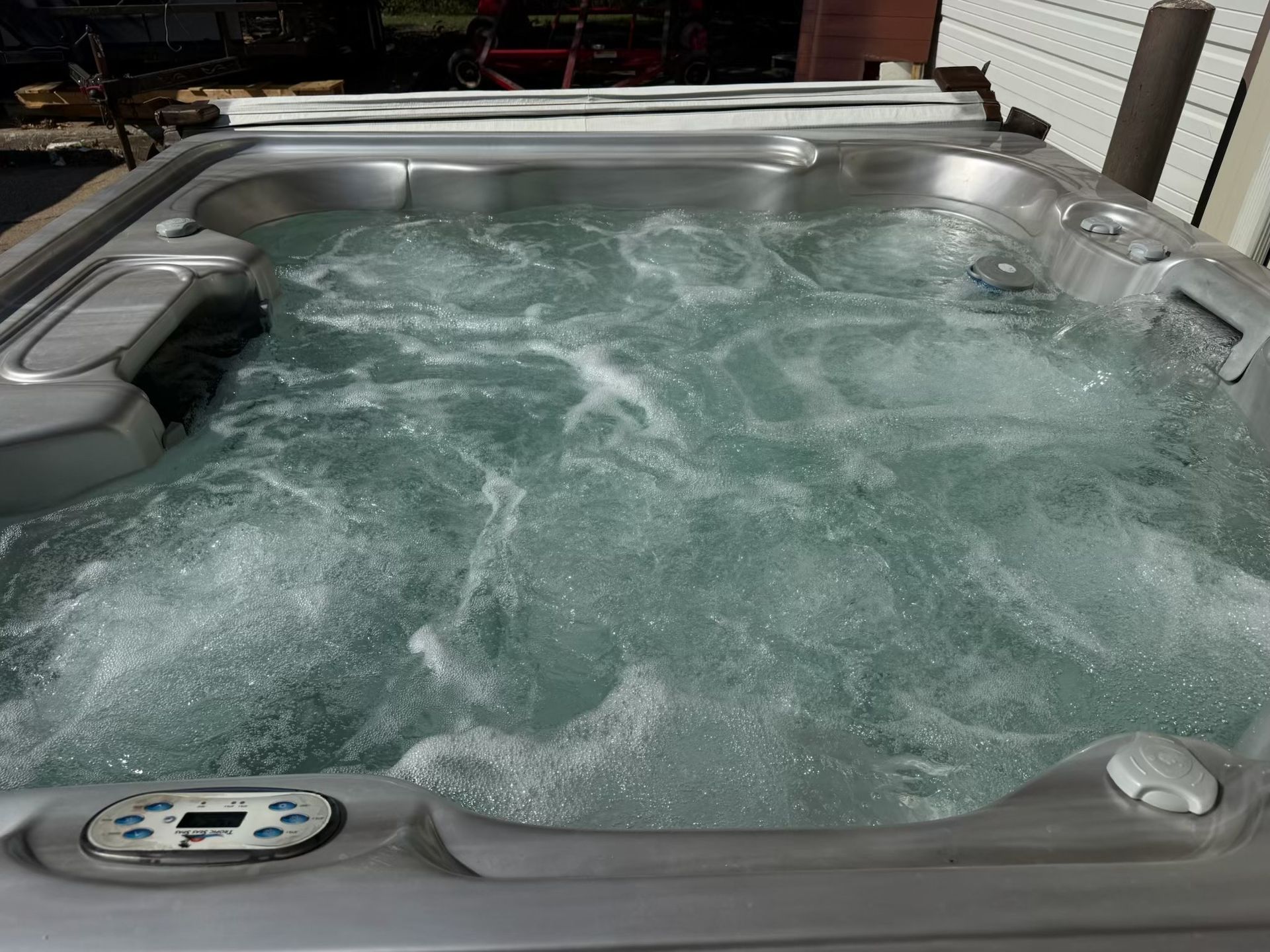 A hot tub filled with bubbling water, partially open, outdoors on a sunny day.