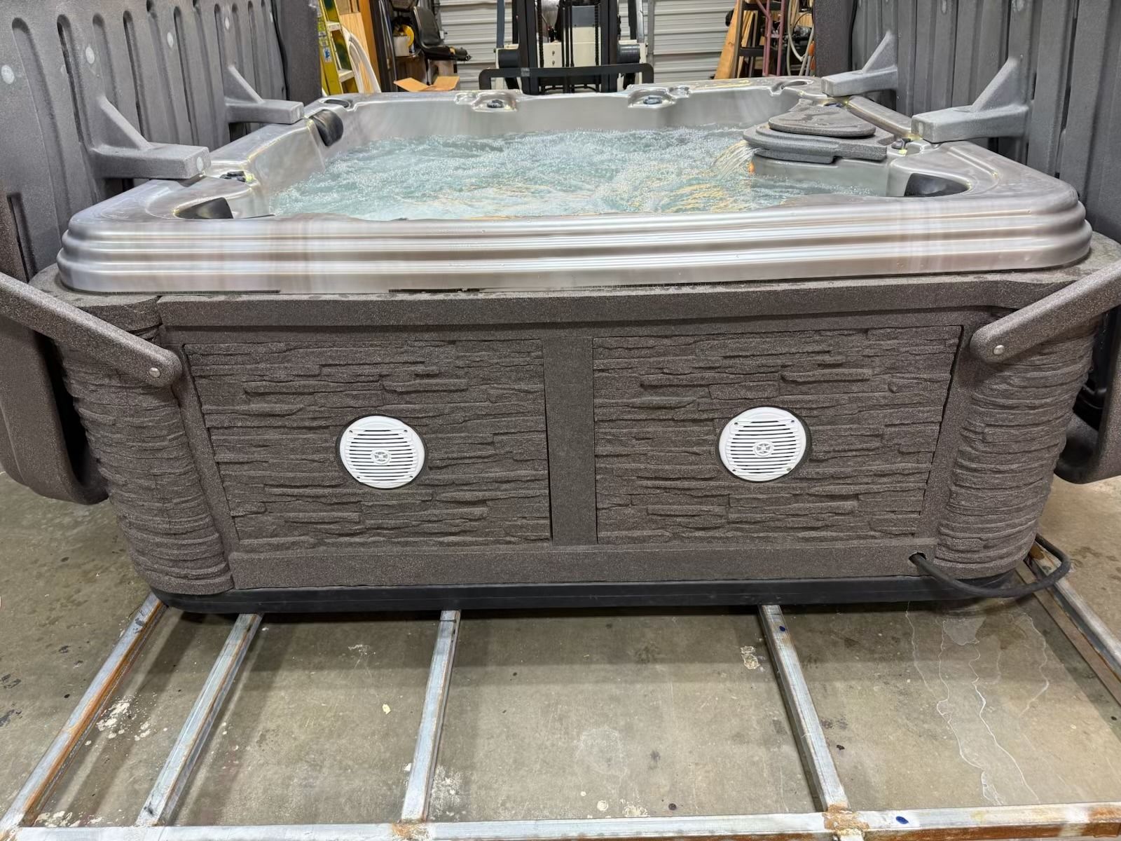 Hot tub being lifted by forklift in a warehouse setting. The tub is filled with water.