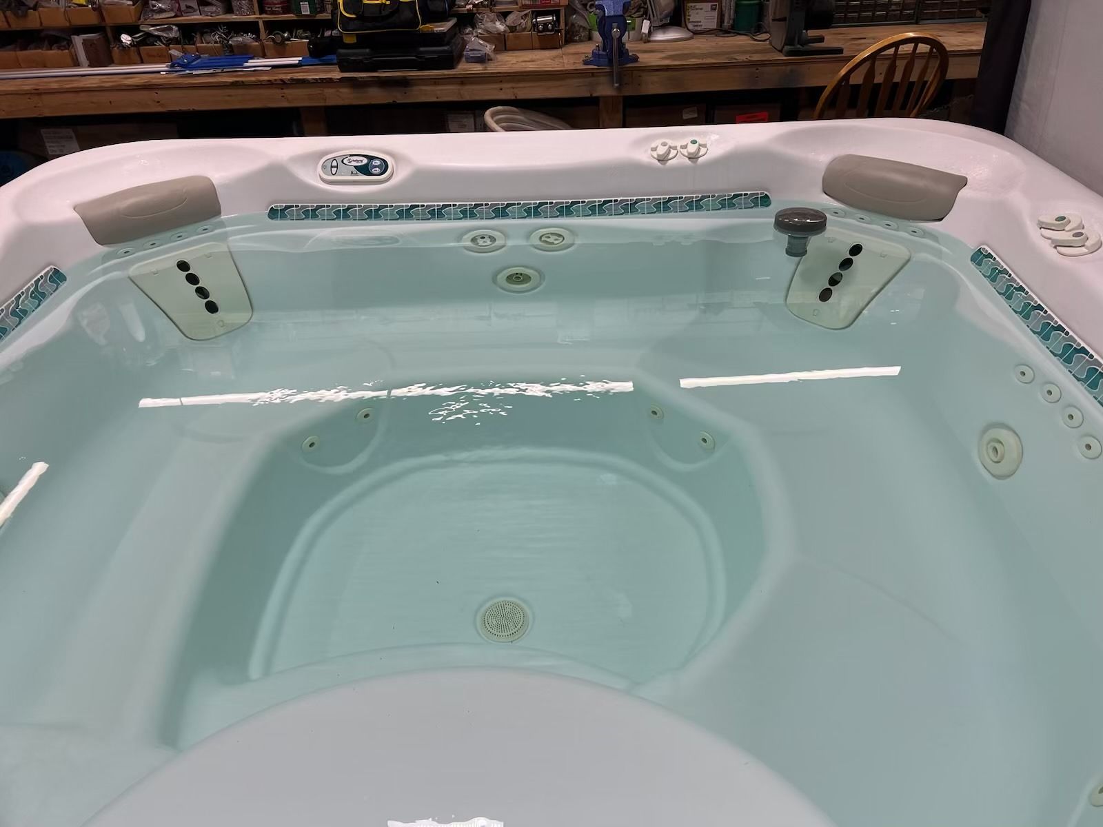 A filled hot tub with teal trim and seating, inside a workshop setting.