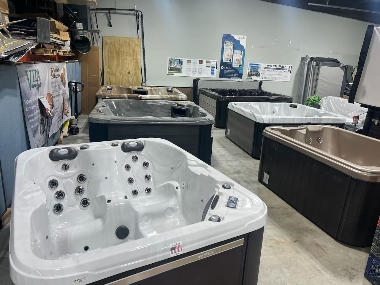 Hot tubs displayed in an indoor showroom setting. Several rectangular tubs in various colors.