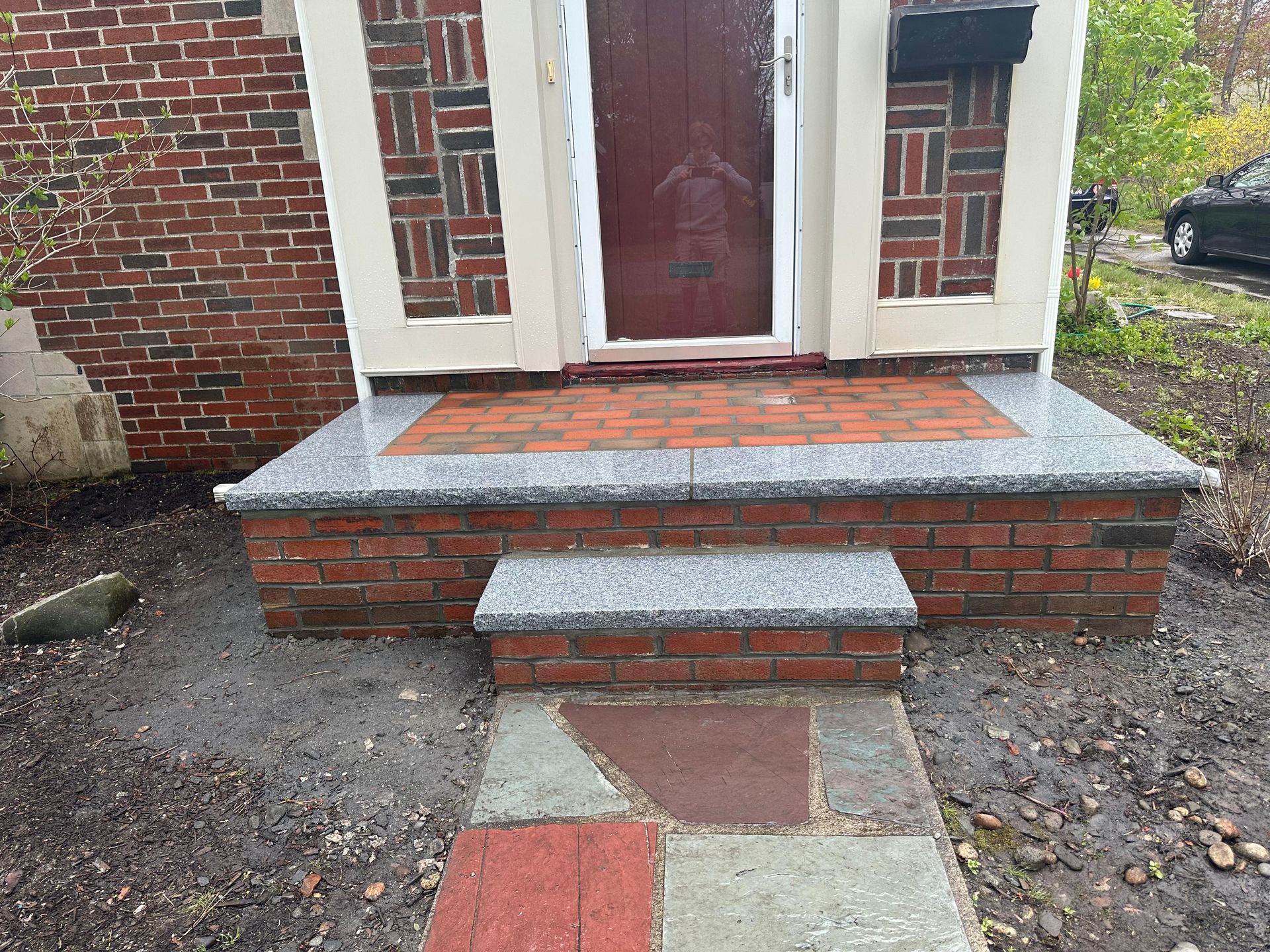 Front entry with brick steps, red door, and a short stone walkway leading to the porch.