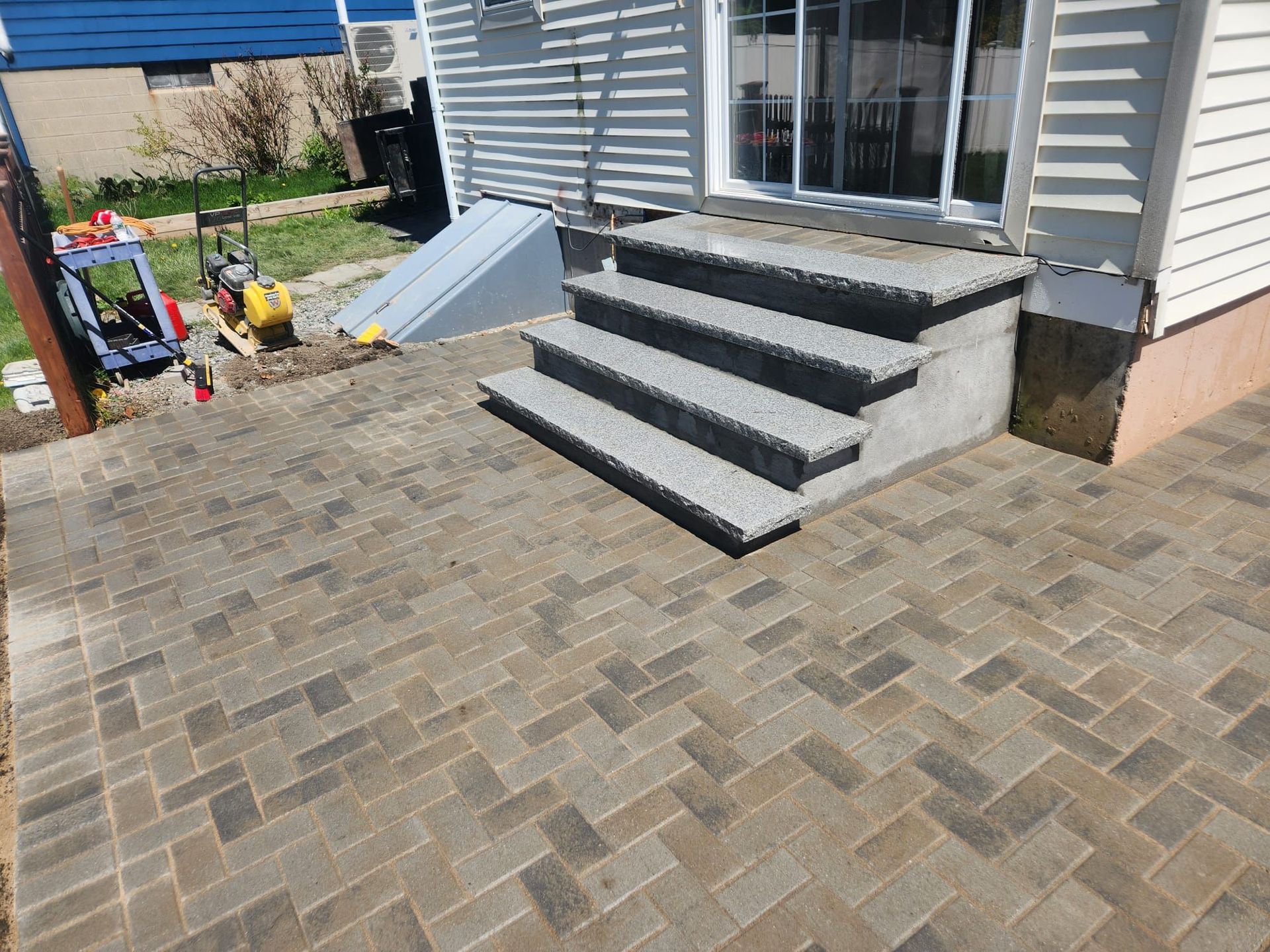 Backyard patio with stone pavers, gray steps, and white siding by a house.
