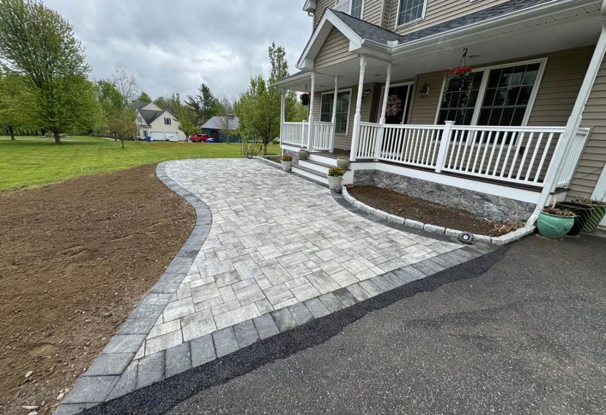 Curved stone walkway leading to a white porch beside a house and asphalt driveway