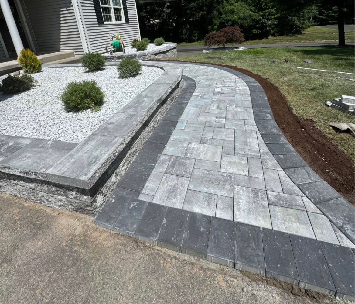 Curved gray stone walkway beside a house, bordered by white gravel and mulch landscaping.