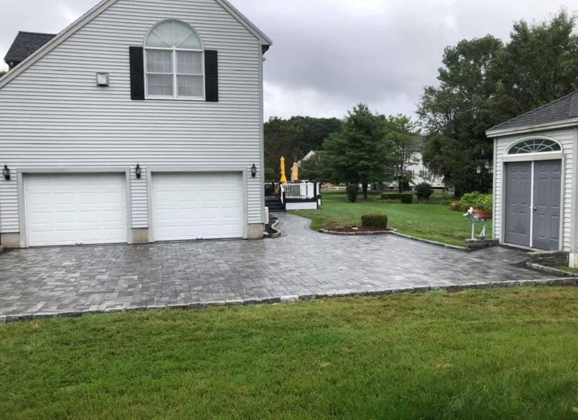 Suburban house with double garage, stone driveway, and a shed beside a wet lawn