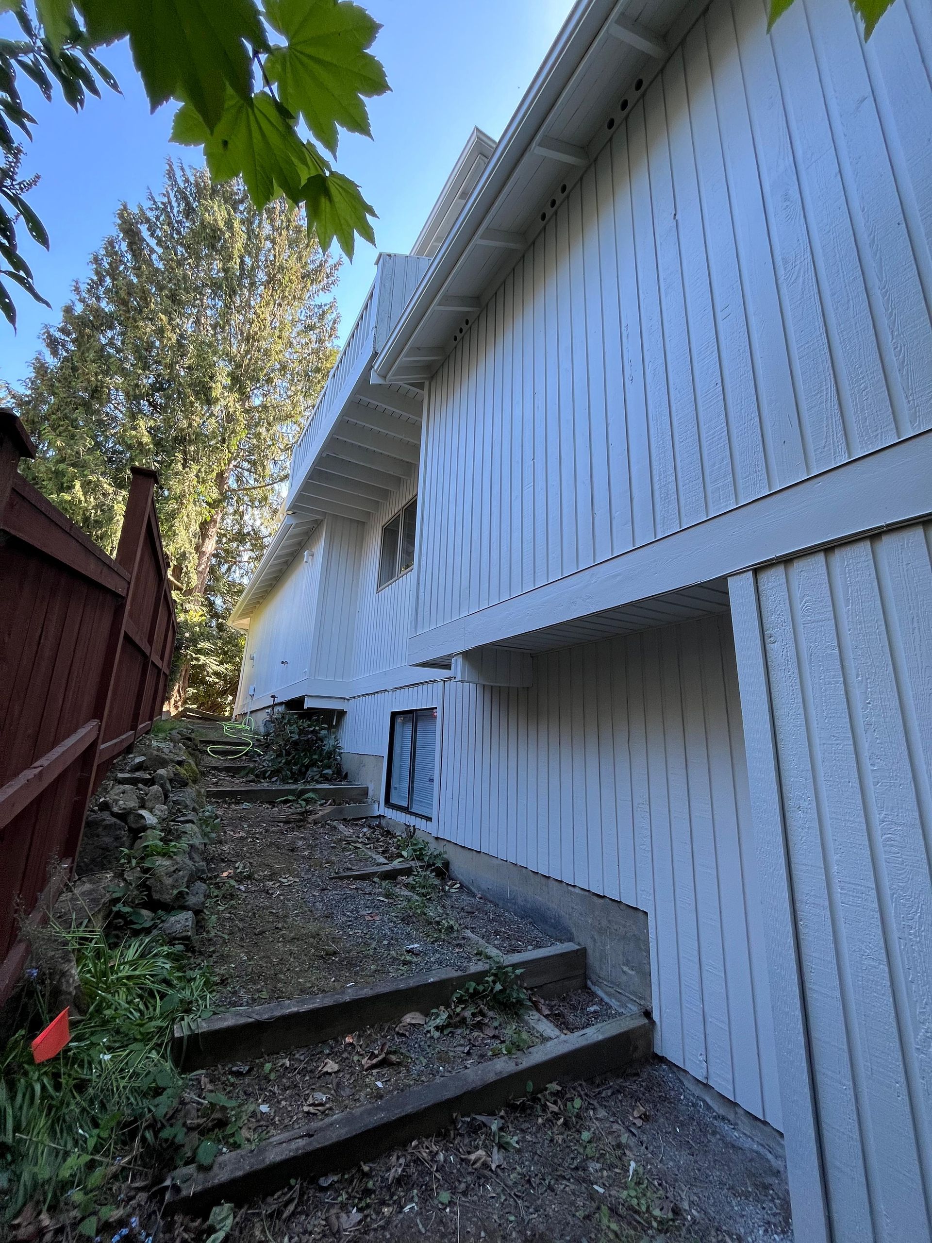 Steep outdoor stairway beside a white house with a red fence and trees overhead