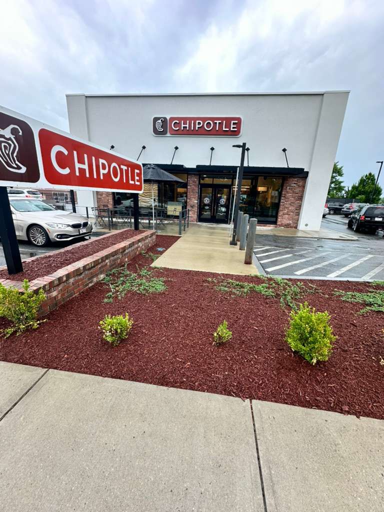 Chipotle storefront with red sign, stone entrance, and parking lot on a cloudy day