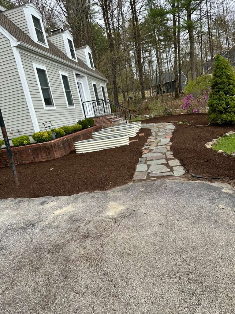 White house exterior with stone walkway, front steps, and landscaped yard beside wooded trees.