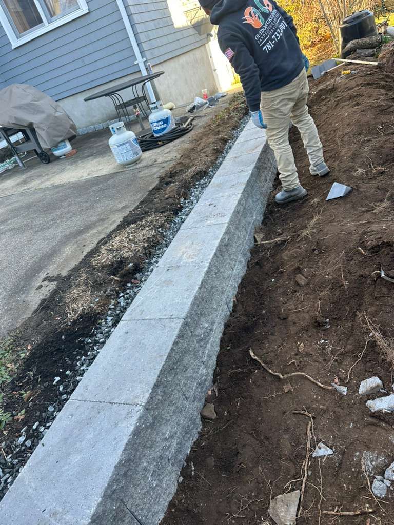 Worker standing beside a long concrete curb in a dirt trench at a construction site