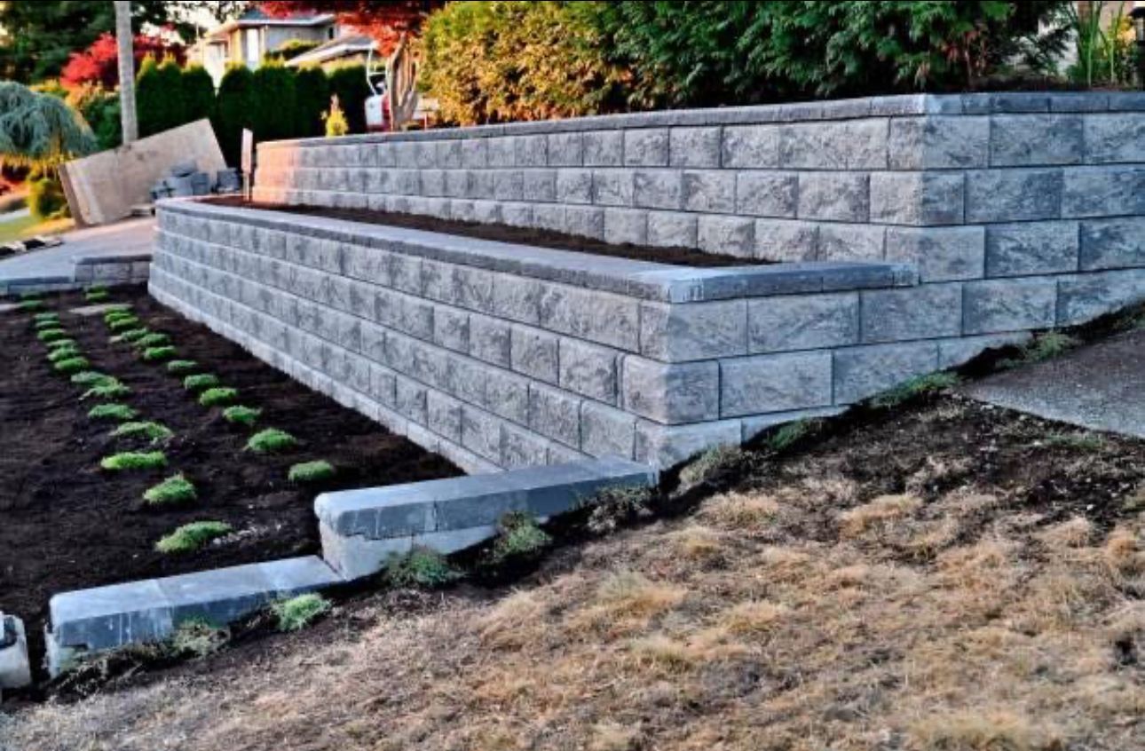 Terraced stone retaining wall with steps beside a landscaped garden and dry grass slope