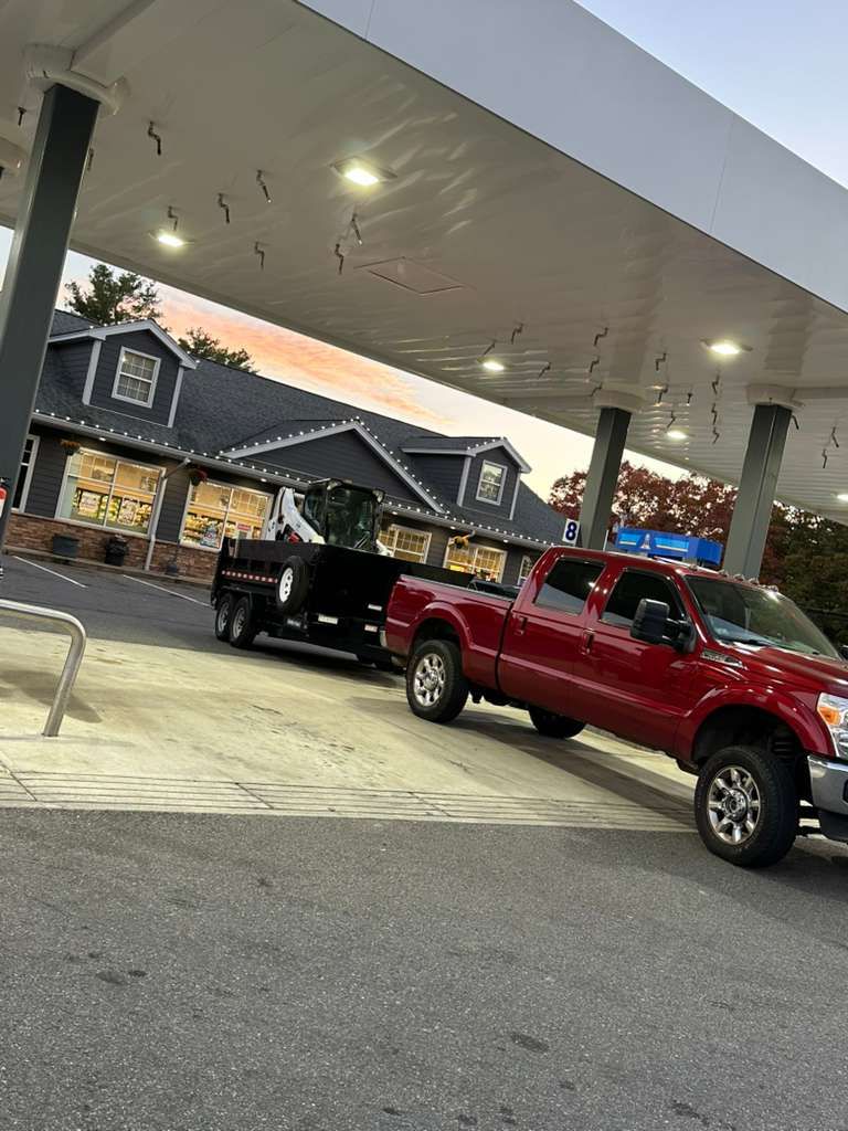 Red pickup truck at a gas station under bright canopy lights, with a black truck beside it at dusk.