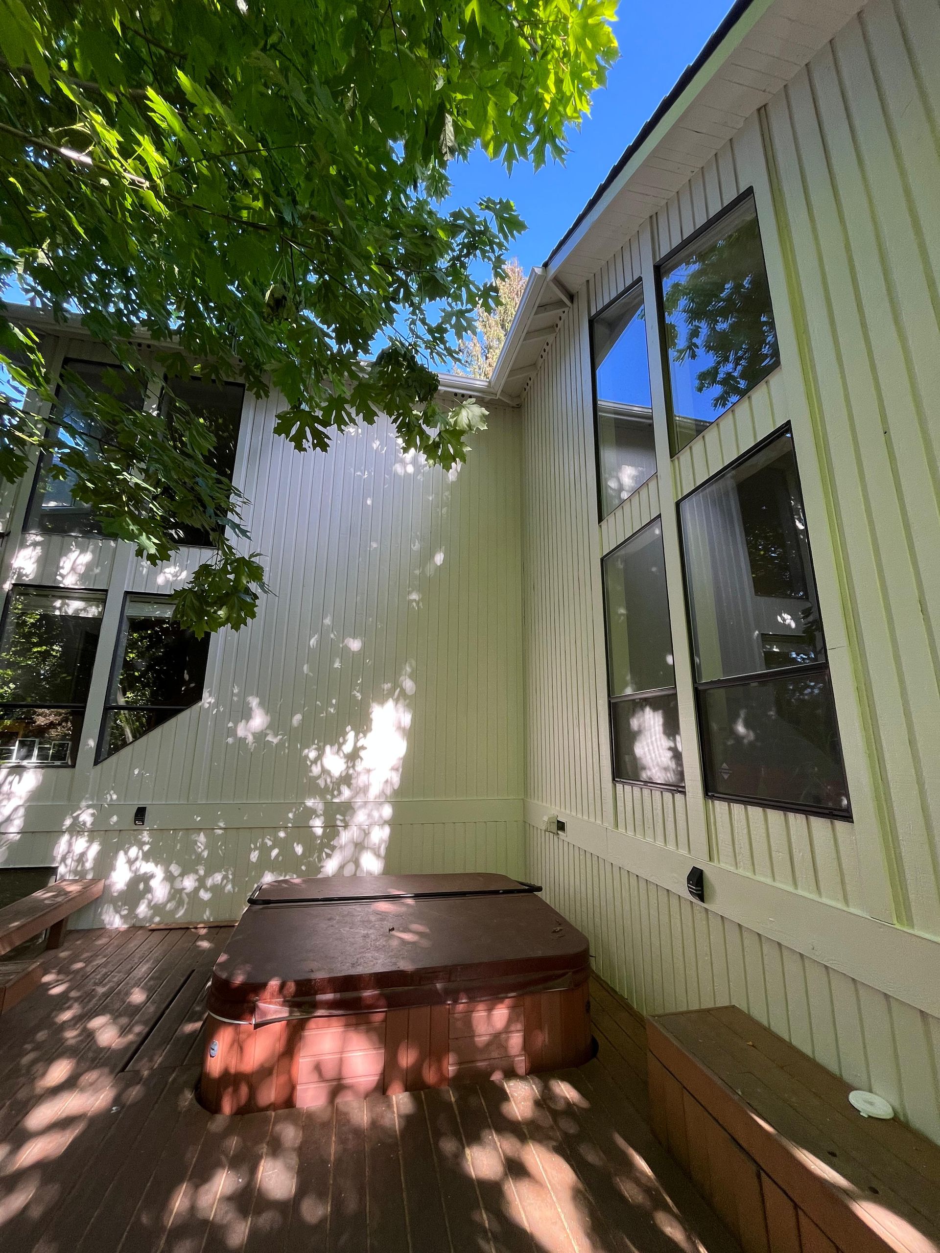 Shaded backyard patio with white siding, windows, and a brick steps leading to a door
