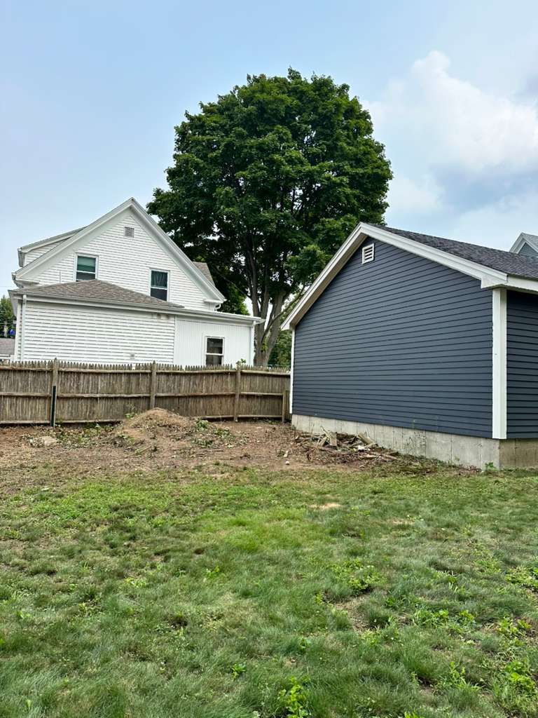 Backyard with a wooden fence, two houses, a large tree, and grass in the foreground