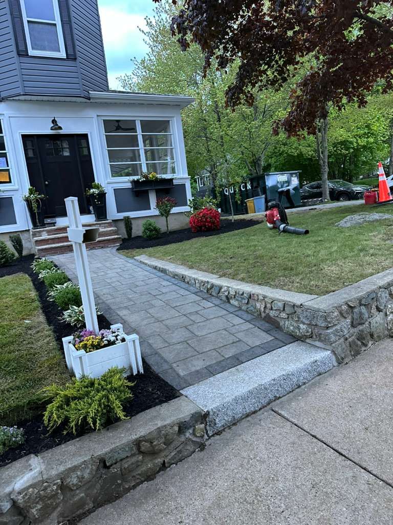 Front walkway to a house with stone steps, flower planters, and a lawn with tools and orange cones