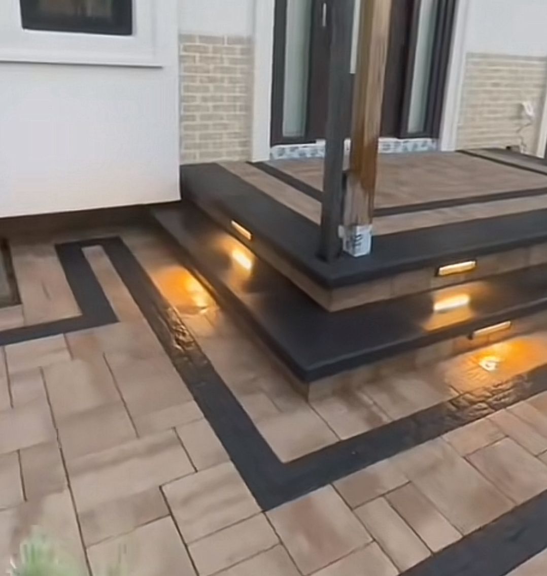 Modern deck with wooden posts, black trim, and warm step lights on a tiled patio
