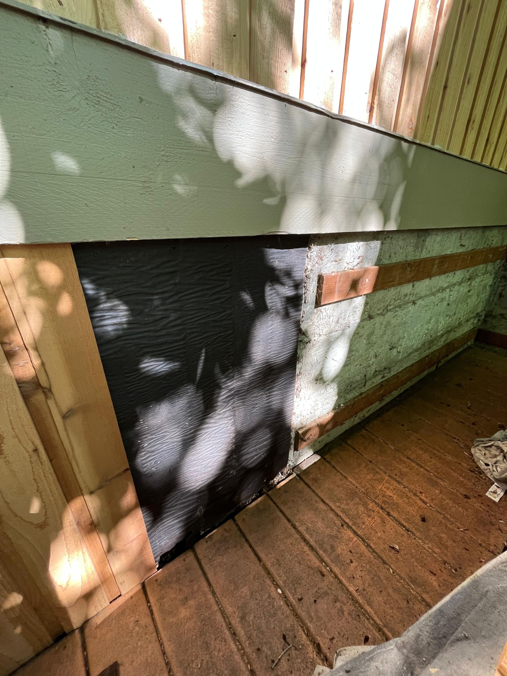 Black panel set into a green wall above a wooden deck, with sunlight and leaf shadows across the surface