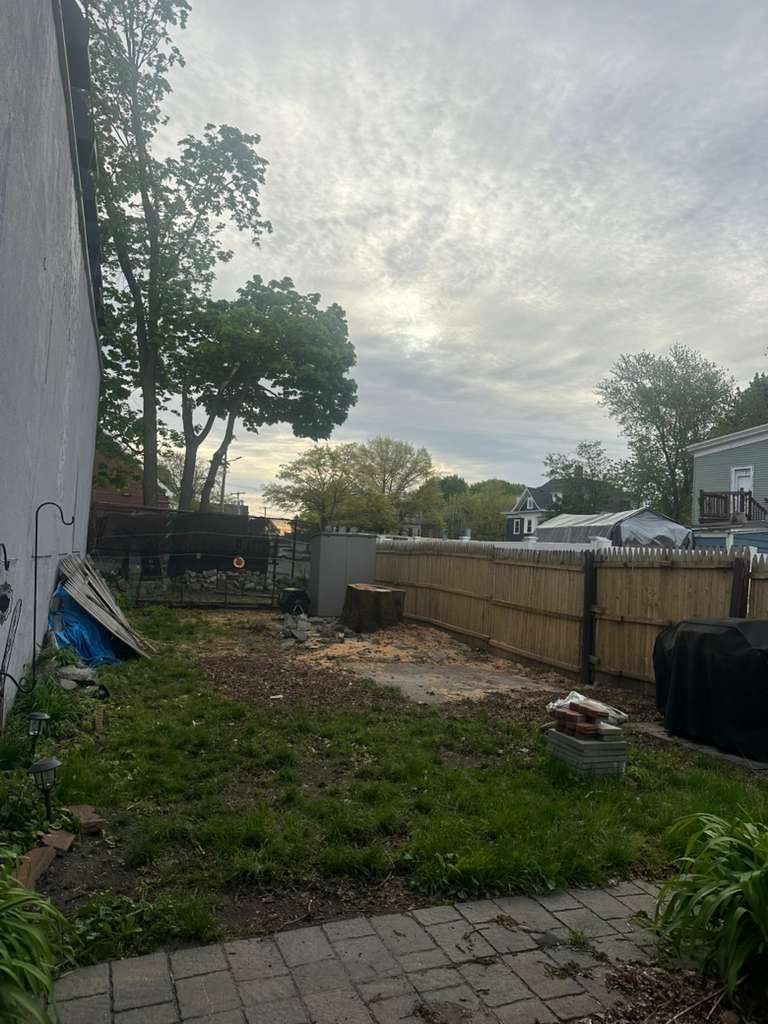 Backyard with concrete patio, wooden fence, trees, and a cloudy sky