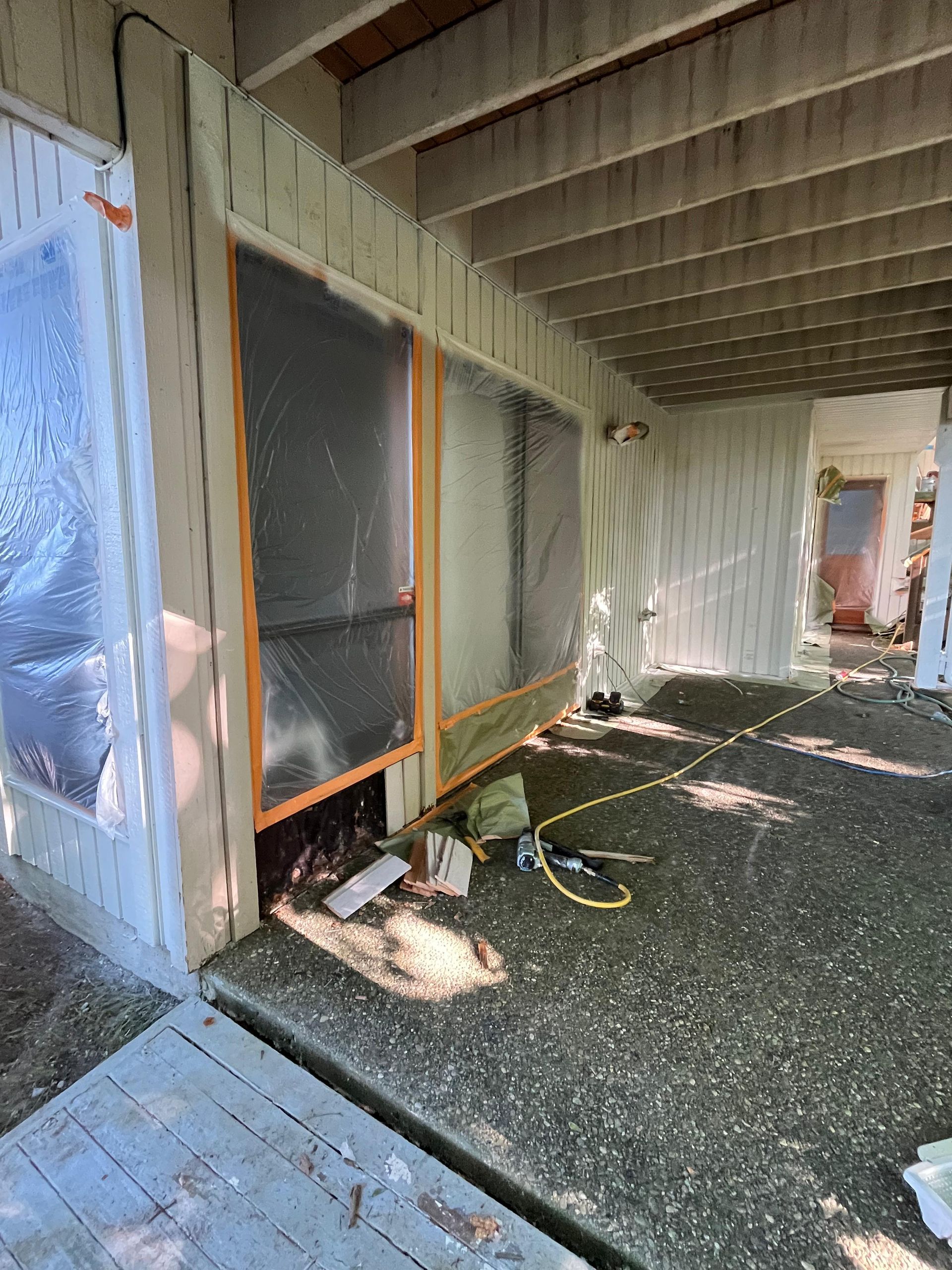 Covered outdoor porch with screened windows, construction materials, and a small dog lying on the ground