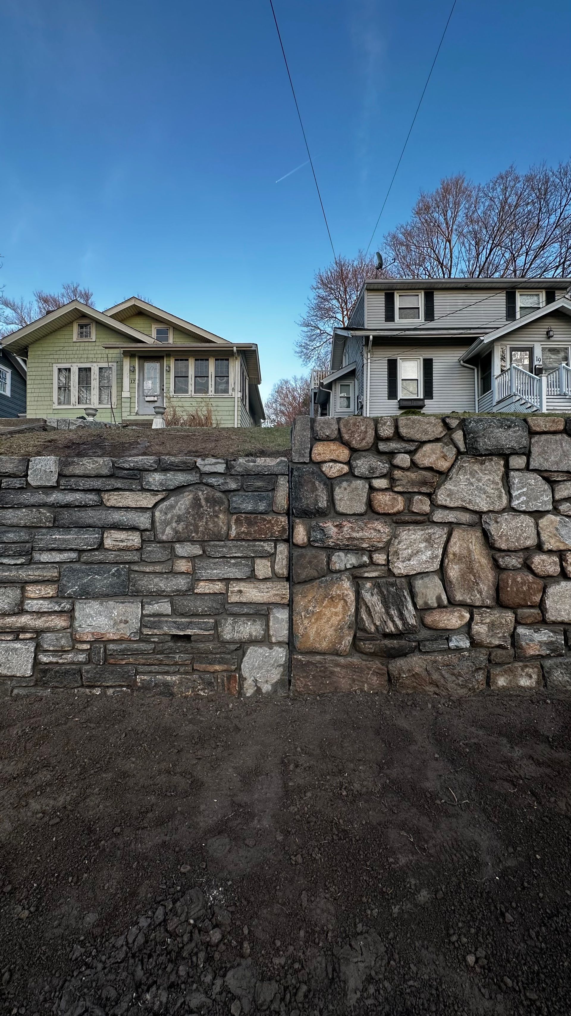 Two houses behind a tall stone retaining wall under a clear blue sky