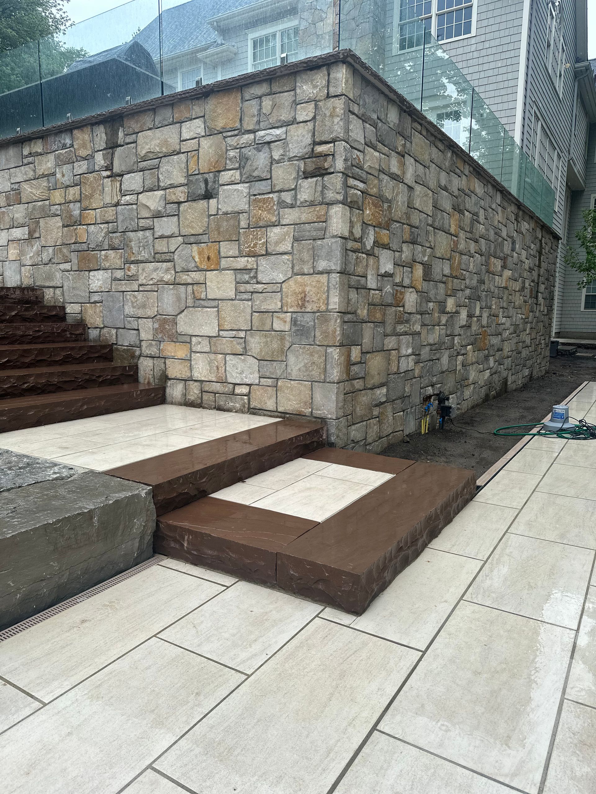 Stone retaining wall beside steps and a paved walkway, with sloped ramp sections outdoors.