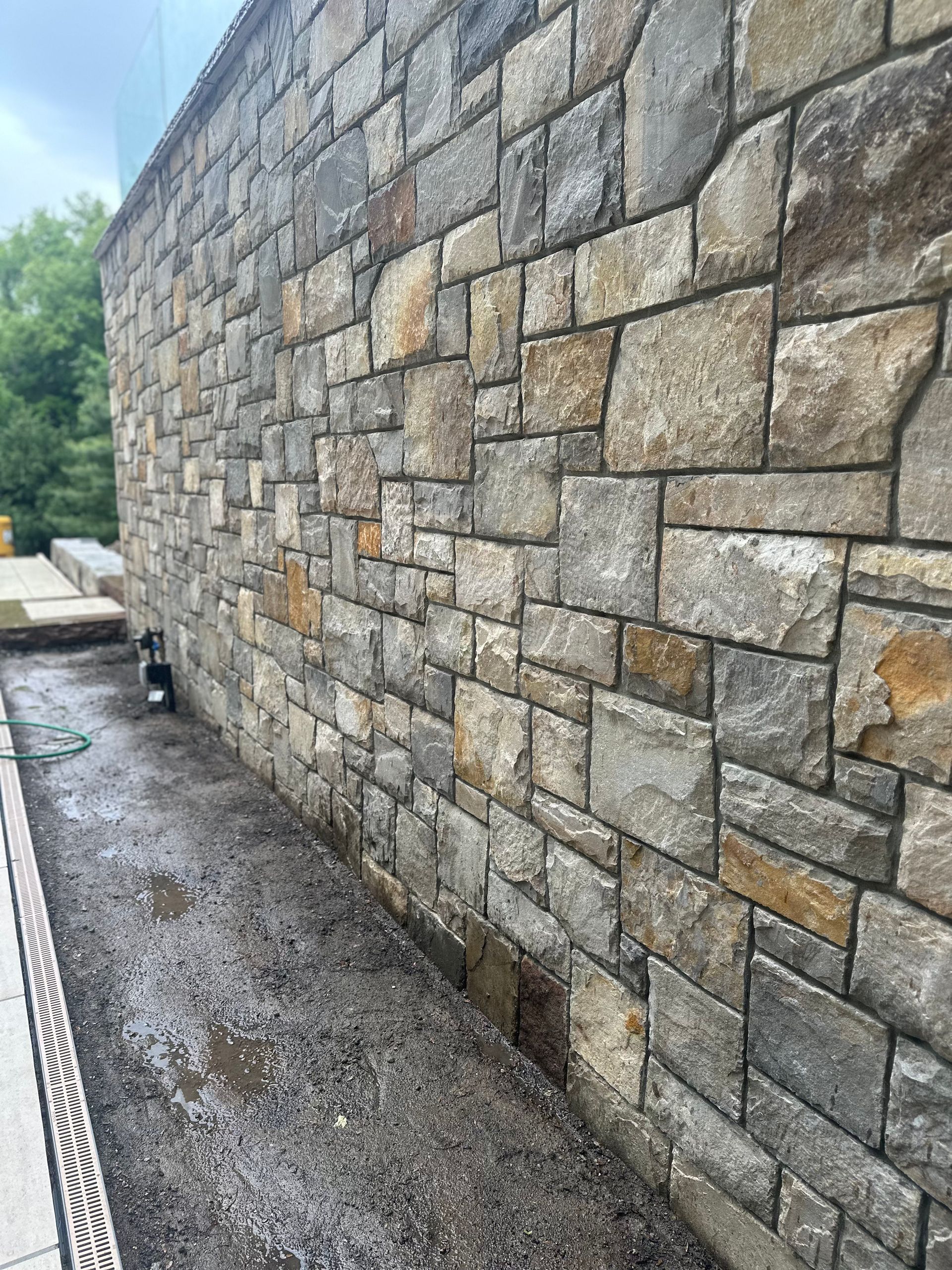 Stone retaining wall beside a wet gravel path, viewed along its length outdoors.