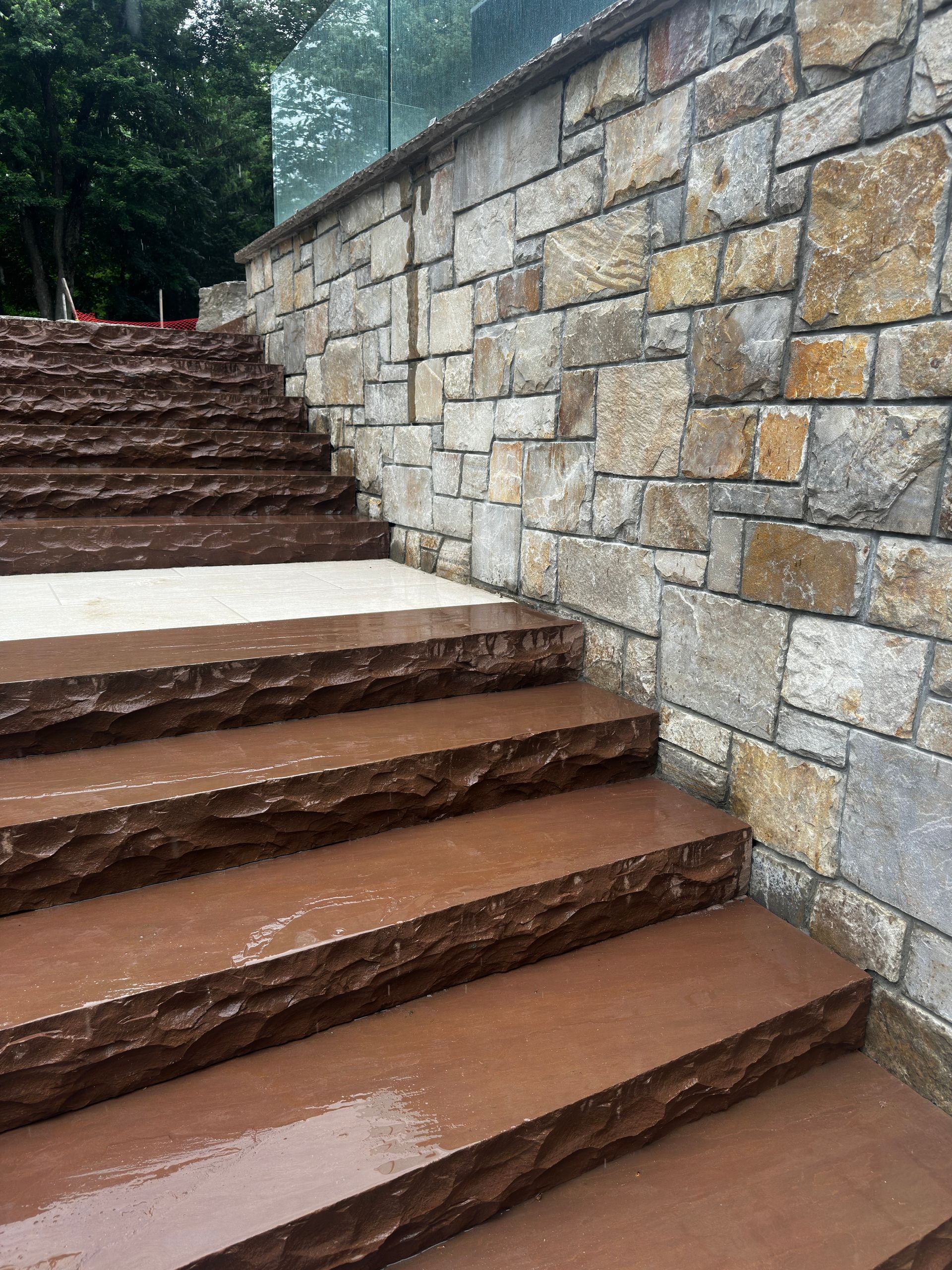 Wet stone steps beside a stone retaining wall in a wooded outdoor area