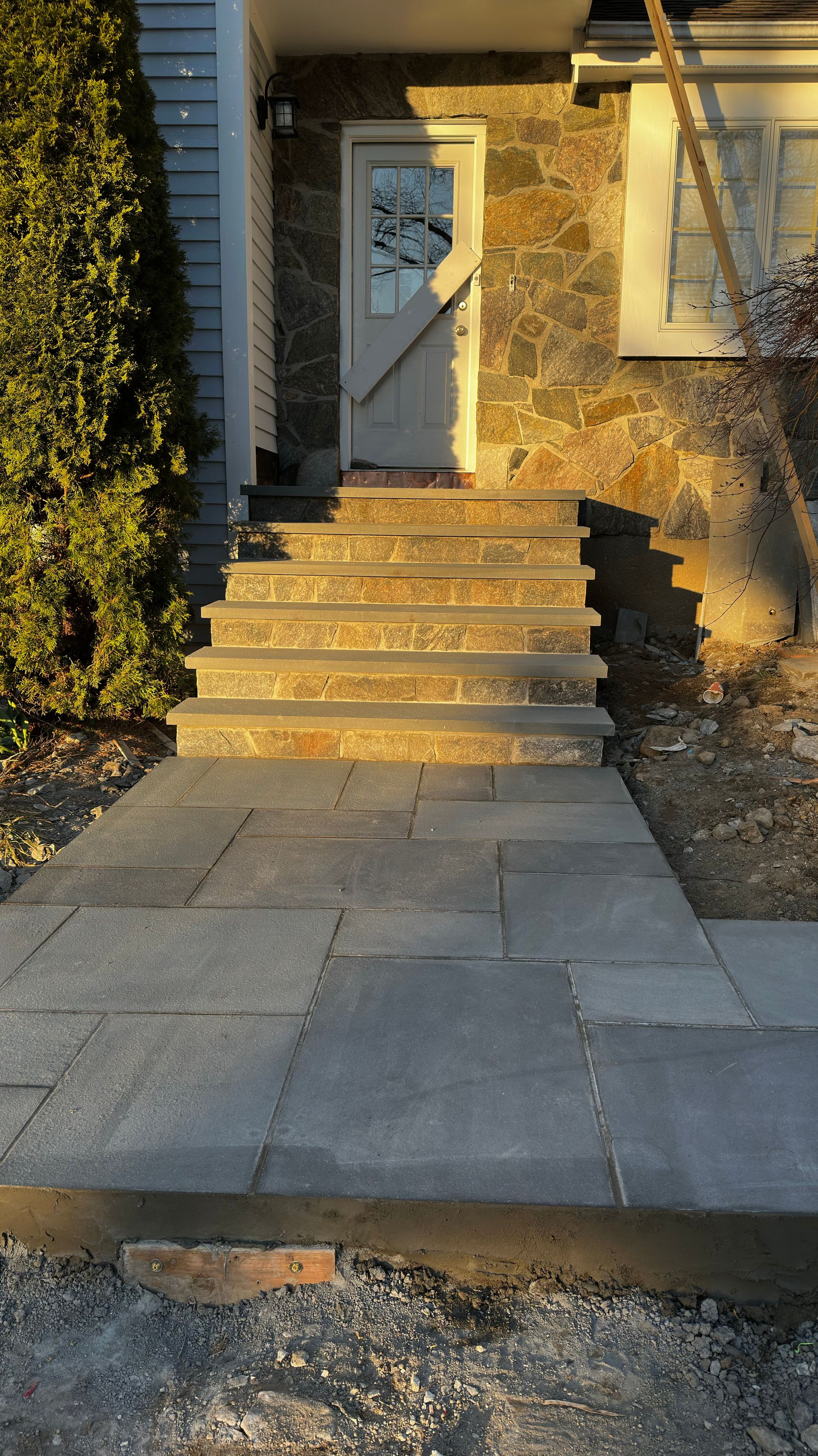 Front steps leading to a white front door beside a stone house in warm sunlight
