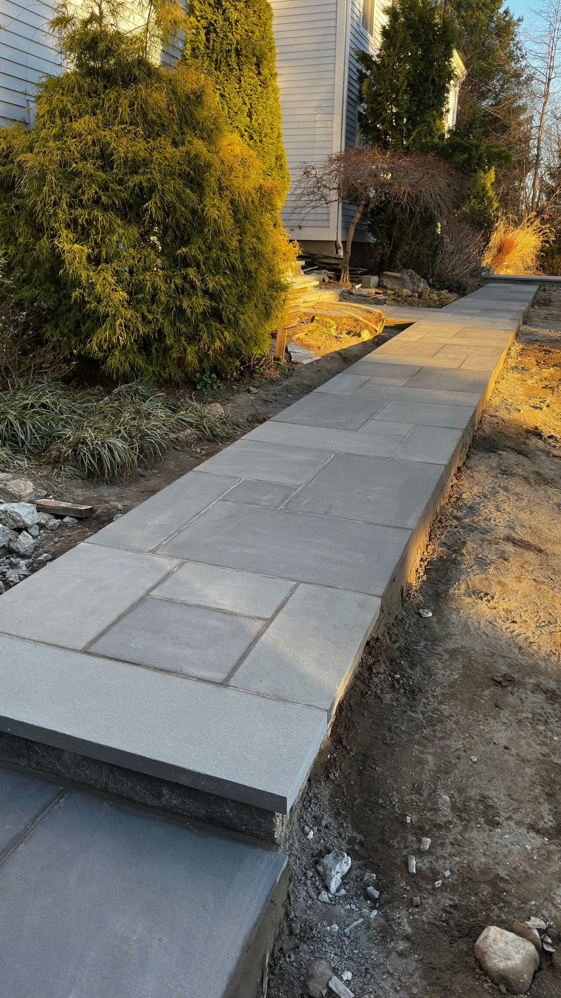 Stone garden path under construction beside shrubs and a house